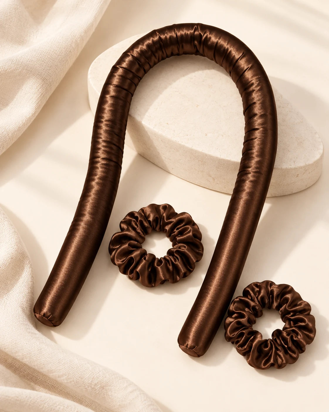 Chocolate brown heatless curling rod and two matching satin scrunchies on an ivory surface