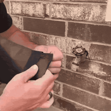 Slipping the insulated cover over an outdoor faucet and securing the strap
